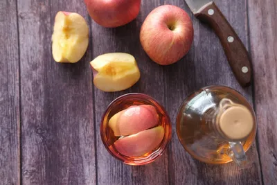 Apple cider vinegar in a glass and bottle with fresh apples on a wooden surface
