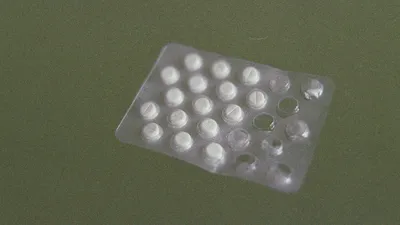 Methenamine hippurate tablets (Hiprex) on a clinical desk beside a urine sample pot, used for recurrent UTI prevention
