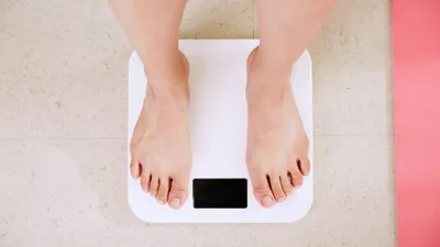 Person stepping onto a bathroom scale, representing the connection between obesity and bladder health