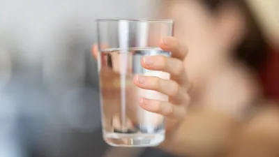 Person drinking a glass of water, supporting bladder health and reducing post-micturition dribble and UTI risk