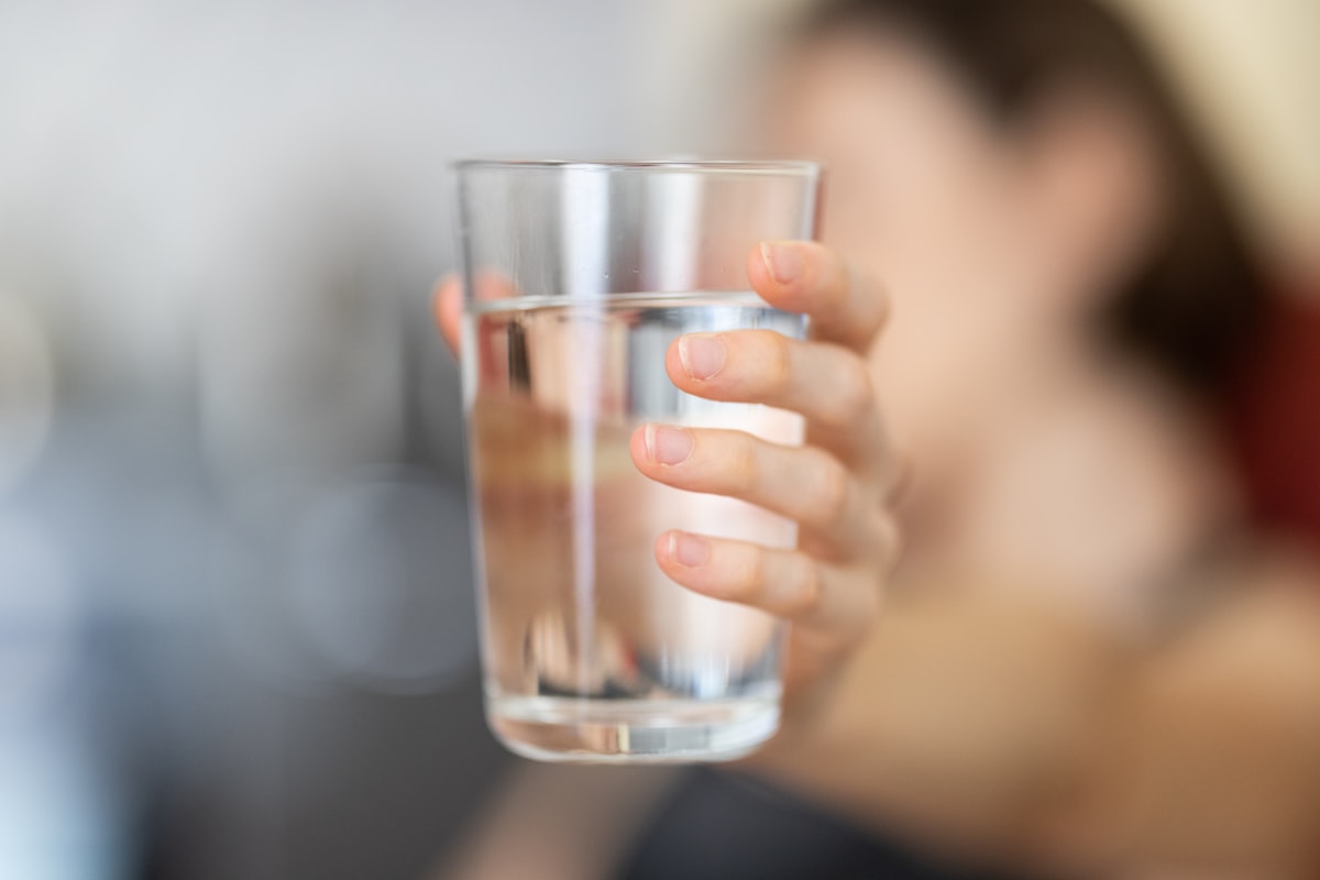 Person drinking a glass of water, supporting bladder health and reducing post-micturition dribble and UTI risk