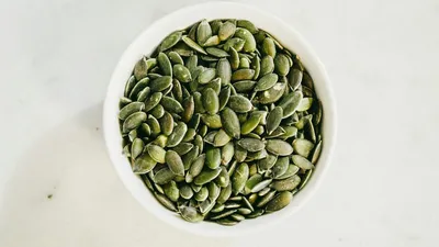 Pumpkin seeds and a glass jar of pumpkin seed extract capsules on a wooden surface, illustrating the difference between forms used for bladder health