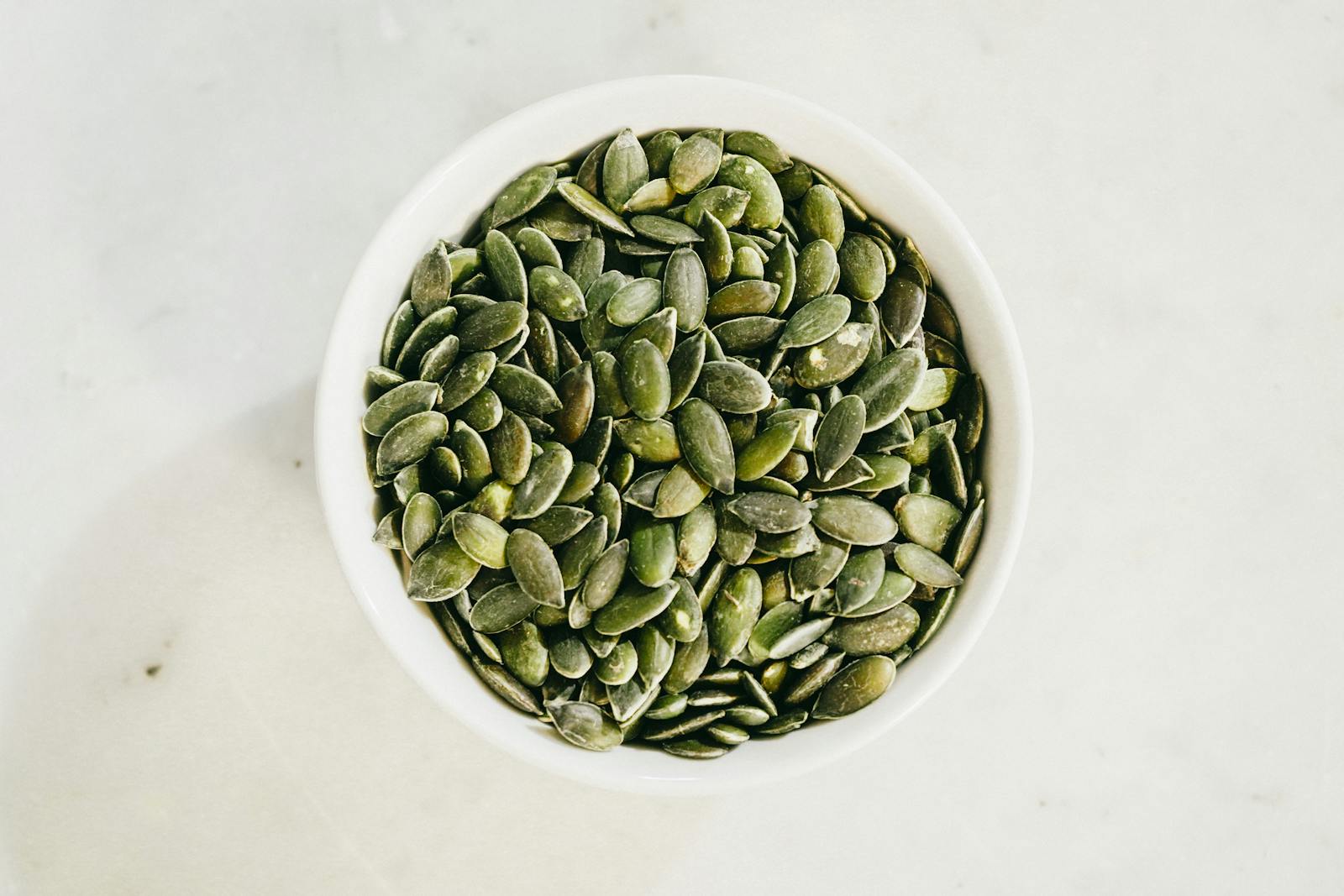 Pumpkin seeds and a glass jar of pumpkin seed extract capsules on a wooden surface, illustrating the difference between forms used for bladder health